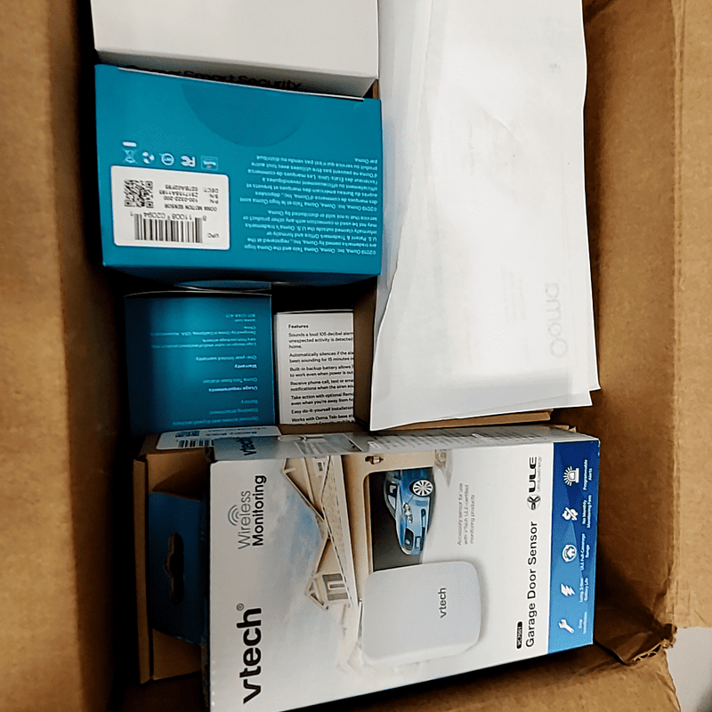 Ooma Smart Home Security System kit displayed in a cardboard box with various sensors and components.