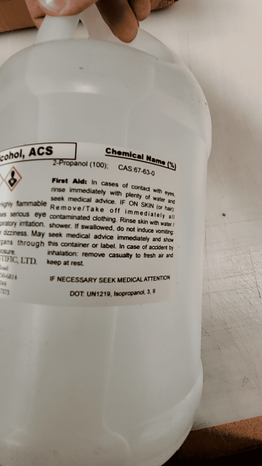 Label on a sealed bottle of Isopropyl Alcohol 99.99% ACS Grade with safety instructions and chemical details.