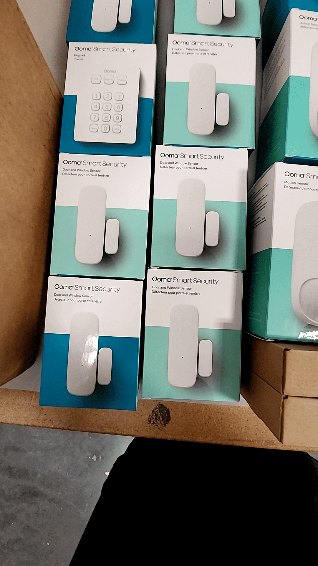 Ooma Smart Security system components including door/window sensors and control panel in packaging.